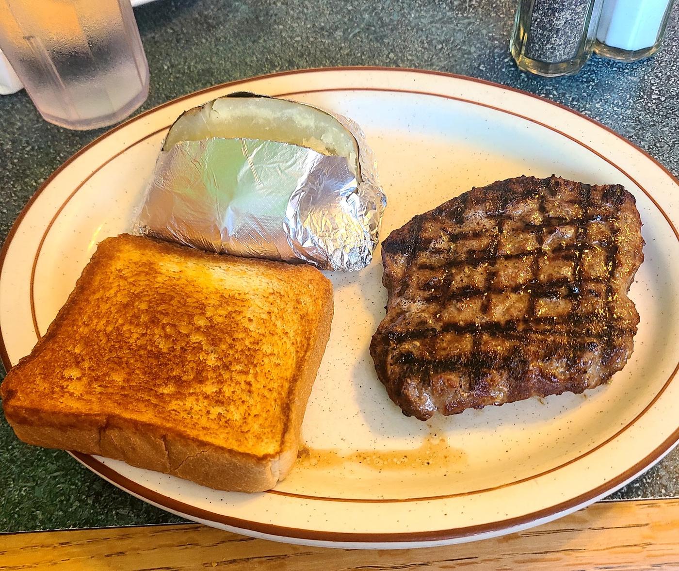 A steak plate with baked potato and toast, viewed from above, at Grecian Steak House